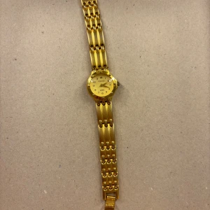 Guldfärgad klocka från Gucci - Säljer en elegant guldfärgad klocka från Gucci. Klockan har en rund urtavla med tydliga siffror och ett stilrent armband i metall. Perfekt för både vardag och fest. Den är i mycket bra skick och ger en lyxig känsla på handleden. Använd 1 gång!