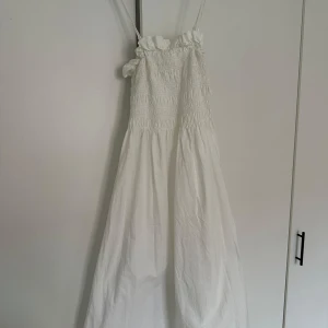 Vit klänning med smockdetaljer - Vit klänning med smala axelband och smockdetaljer upptill. Axelbanden kan hakas av om man vill ha bandeauklänning. Jättefint skick och inte genomskinlig. Strl XS men passar mig som har S