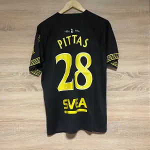 Snygg svart AIK fotbollströja från Nike med gula detaljer och nummer 28 på ryggen. Tröjan har korta ärmar med mönstrade kanter och AIK:s emblem på bröstet. Perfekt för alla AIK-fans!