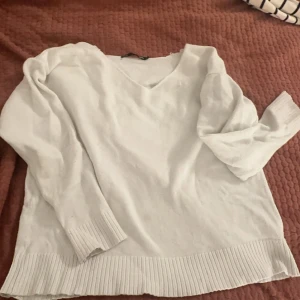 Vit stickad tröja från 157 - Mysig vit stickad tröja från 157 med v-ringning och ribbade kanter. Perfekt för kyliga dagar och enkel att matcha med olika outfits.