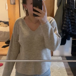 Beige stickad tröja - Mysig beige stickad tröja med v-ringning. Perfekt för kyliga dagar och passar både till vardags och lite finare tillfällen. Tröjan har långa ärmar och en skön passform som inte sitter för tight. Ett måste i garderoben för höst och vinter!