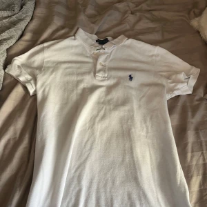 Vit pikétröja från Ralph Lauren - Säljer en klassisk vit pikétröja från Ralph Lauren i bra skick. Den är i storlek 158-164. Knappas använd! Den har en broderad blå logga på bröstet och knappar vid kragen. Perfekt för en stilren och avslappnad look. Passar både till vardags och festliga tillfällen! 
