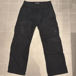 Svarta cargobyxor från Brandit - Säljer ett par svarta cargobyxor från Brandit med justerbart bälte. Lite slitage vid hälen, men annars inga skador. Pris kan diskuteras