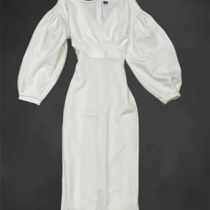 Vit klänning från Shein - Elegant vit klänning från Shein med omlott-design och långa puffärmar. Tillverkad i mjuk polyester med en liten andel elastan för stretch. Perfekt för en stilren look.
