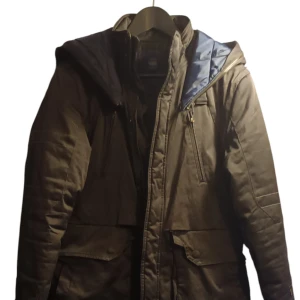 Svart parkajacka från G-Star RAW - Snygg svart parkajacka från G-Star RAW med huva och dragkedja. Jackan har flera praktiska fickor och är perfekt för kyligare väder. Den är designad för att hålla dig varm och bekväm under höst och vinter. Sömmen är lite sprucken vid fickan, går att sy.