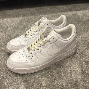 Vita Nike Air Force 1 - Snygga och klassiska vita Nike Air Force sneakers med snörning. Perfekta för en stilren look och bekväma att bära hela dagen.