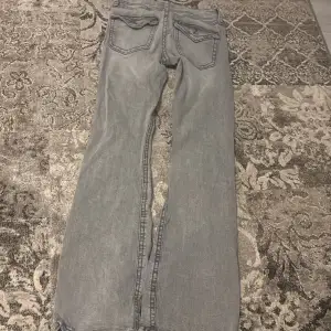 Säljer ett par grå jeans från Gina Tricot. De har en klassisk femficksdesign och en bootcut-stil som ger en snygg siluett. Perfekta för en avslappnad look.