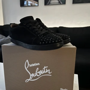 Svarta sneakers med nitar från Christian Louboutin - Säljer ett par svarta sneakers från Christian Louboutin i bra skick. Skorna har coola nitar på tån och den klassiska röda sulan.