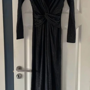 Svart glittrig jumpsuit  - Snygg svart jumpsuit med glittrigt mönster och omlott-design. Den har långa ärmar och en elegant drapering framtill som ger en smickrande passform. Perfekt för festliga tillfällen när du vill glänsa lite extra! ✨väldigt fint skick