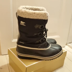 Svarta vinterstövlar från Sorel - Säljer ett par svarta Sorel vinterstövlar i bra skick endast använda på en skidresa. De är fodrade med mjuk päls och har snörning framtill. Perfekta för kalla vinterdagar med sin vattentäta design. Stövlarna har en robust sula för bra grepp på isiga underlag.