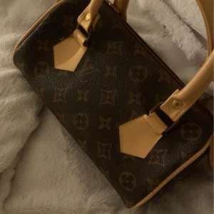 Brun handväska med monogram - Säljer en snygg brun handväska med klassiskt monogrammönster. Väskan har ljusa läderdetaljer och guldiga metalldelar. Perfekt för både vardag och fest! 👜✨