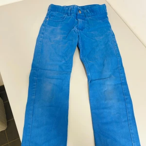 Blå byxor från H&M - Säljer ett par snygga blå byxor från H&M i storlek för barn 10-11 år. Byxorna har en klassisk design med knapp och dragkedja framtill. Perfekta för både vardag och festliga tillfällen. De är i bra skick och redo för en ny ägare!