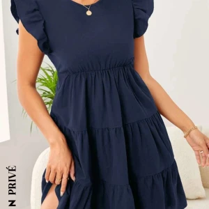 Mörkblå klänning med volangärmar - Snygg mörkblå klänning med volangärmar och rund hals. Perfekt för både vardag och festliga tillfällen. Den har en luftig passform och är gjord i ett mjukt material som faller fint. Klänningen har en knäppning i nacken och är knälång.