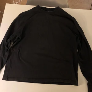 Svart långärmad tröja från New Garments - Säljer en svart långärmad tröja från New Garments i 100% bomull. Den är i bra skick och har en diskret broderad smiley på framsidan. Perfekt för höst och vinter, och passar till alla tillfällen. Skön och stilren design!