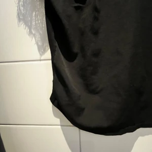 Svart topp med spetsdetaljer - Snygg svart topp med spetsdetaljer på axlarna och en klassisk krage. Perfekt för en kväll ute eller en fest. Toppen har en normal passform och är tillverkad i ett mjukt material som känns skönt mot huden.