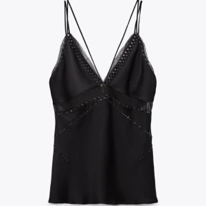 Svart sidenlinne med spetsdetaljer - Elegant svart sidenlinne med tunna axelband och spetsdetaljer. Linnet har en djup v-ringning och små nitar längs kanterna för en extra touch. Storlek M, passar s/m.