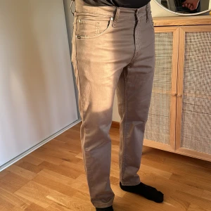 Beige jeansbyxor - Säljer ett par snygga beige byxor i mycket bra skick. De har en normal passform och är perfekta för både vardag och fest. Byxorna har en klassisk femficksdesign med dragkedja och knapp framtill. Materialet är mjukt och bekvämt, vilket gör dem sköna att bära hela dagen. Jag är 179cm lång och väger 77-78kg
