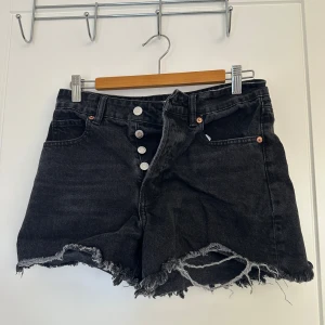 Svarta jeansshorts från H&M - Säljer ett par  svarta jeansshorts från H&M i storlek M. De är högmidjade med knappar framtill och har en snygg fransig kant nertill. Perfekta för sommaren och ger en avslappnad look. Passar både till vardags och fest!