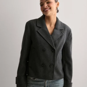 Mörkgrå kappa - Snygg mörkgrå kappa med dubbelknäppning. Perfekt för höst och vinter, med en klassisk look som funkar både till vardags och fest. Den har långa ärmar och en stilren krage. Passar bra till jeans för en avslappnad men chic stil. Köpt för 800kr