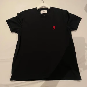 Amir Paris T-shirt  - Snygg svart t-shirt från Amir Paris med ett litet rött hjärta broderat på bröstet. Perfekt för en stilren look. Kortärmad och i normal passform storlek S.