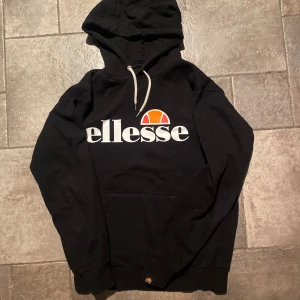 Svart hoodie Ellesse - Säljer en svart hoodie från Ellesse i storlek M. Sitter tajt så snarare som en small. Den har en stor logga på framsidan och en justerbar huva med vita snören. Perfekt för en avslappnad stil eller träning. Bra skick!