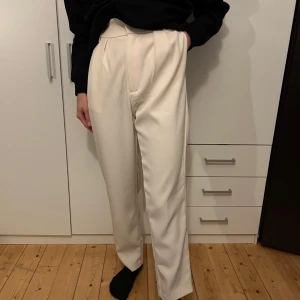 Beige kostymbyxor - Säljer ett par stilrena beige kostymbyxor i mycket bra skick. De är högmidjade med en rak passform som ger en elegant look. Perfekta för både kontoret och festligare tillfällen. Materialet känns mjukt och bekvämt mot huden.