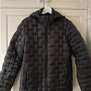 Svart dunjacka från Everest - Säljer en svart dunjacka från Everest i mycket bra skick. Jackan har en dragkedja och huva, storlek 170/176. Perfekt för kalla vinterdagar. Den är långärmad och håller dig varm och bekväm. Passar både till vardags och utomhusaktiviteter.