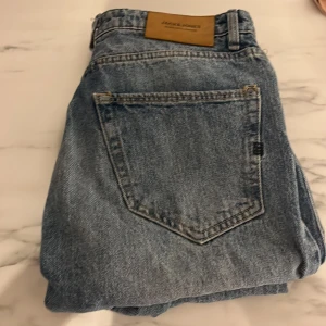 Blå jeans från Jack & Jones - Säljer ett par klassiska blå jeans från Jack & Jones i bra skick. De har en normal passform och är perfekta för vardagsbruk. Jeansen har en traditionell femficksdesign och en snygg läderpatch med loggan på baksidan. Perfekta för både höst och vår!