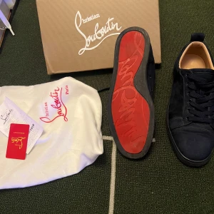 Christian Louboutin  - Snygga svarta sneakers i mocka från Christian Louboutin med den ikoniska röda sulan. Skorna har snörning och en stilren design som passar perfekt för den modemedvetna. Levereras med originalförpackning och dustbag. kvitto finns