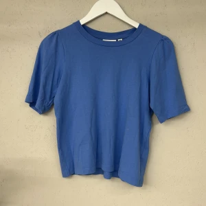 Blå t-shirt från Kappahl - Säljer en enkel och stilren blå t-shirt från Kappahl i storlek XS. T-shirten har korta ärmar och en rund halsringning. Perfekt för en avslappnad look. Någon liten fläck men inget som läggs märke till.