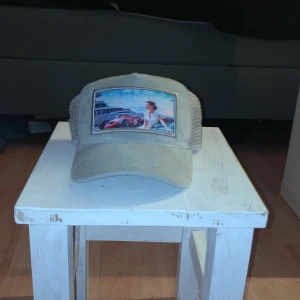 Grå keps med tryck  - Snygg beige keps från Revenite med ett coolt tryck på framsidan. Kepsen har ett nätmaterial på baksidan för bättre ventilation och en justerbar rem för perfekt passform. Kepsen är limited edition och det säljs inte några av dem exemplaren mer