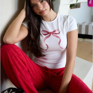 Vit t-shirt med rosett - Söt vit t-shirt från Nelly med ett tryck av en rosa rosett på framsidan. Den har en klassisk rund hals och korta ärmar, perfekt för en avslappnad stil. Kolla sista bild för bild på liten liten fläck. 