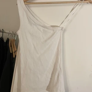 Vit ribbad oneshoulder topp - Säljer en stilren vit ribbad oneshoulder topp. Perfekt för en trendig look med sin asymmetriska design och smala axelband. Passar bra till både jeans och kjol.