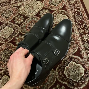 Svarta skinnskor med spännen - Eleganta svarta skinnskor med dubbla spännen och spetsig tå. Perfekta för en stilren look. Storlek 44.