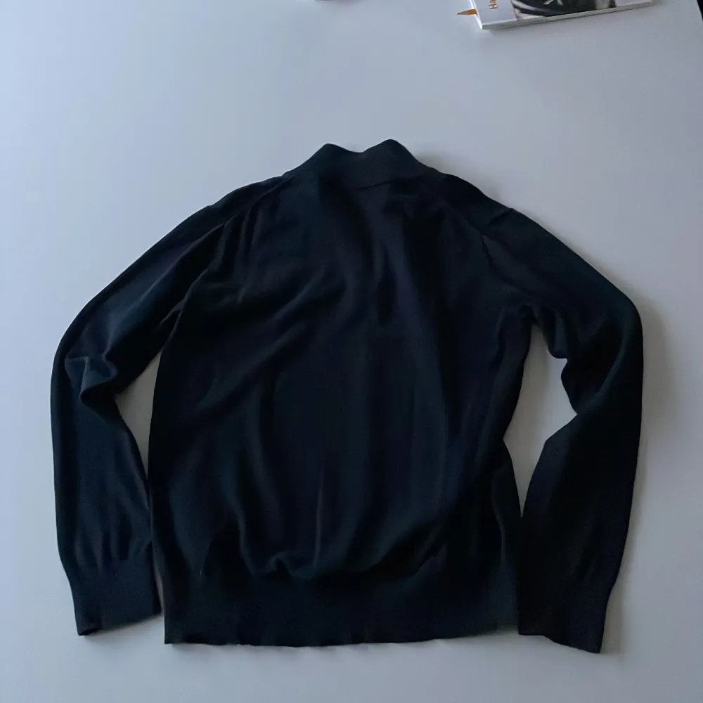 Snygg svart tröja från Gant med dragkedja vid halsen. Perfekt för en stilren look. Tröjan har långa ärmar och en liten logga på bröstet. . Neuletakit & Villapaidat.