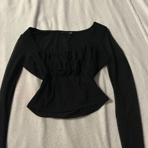Svart långärmad topp från ASOS DESIGN - Snygg svart topp från ASOS DESIGN med långa ärmar i ett transparent material. Toppen har en elegant design med rynkade detaljer framtill som ger en fin passform. Perfekt för en stilren look.