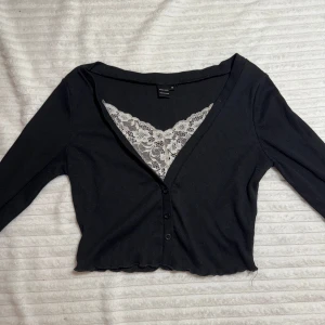 Svart ribbad kofta med spetsdetalj - Säljer en svart ribbad kofta med v-ringning och spetsdetalj vid halsen. Koftan har knappar framtill. Perfekt för en ”Elena Gilbert”- Look!