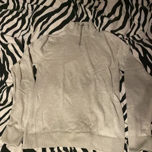 Vit tröja med dragkedja från Jack & Jones - Säljer en stilren vit tröja från Jack & Jones med dragkedja vid halsen. Tröjan har långa ärmar och ribbade muddar vid ärmslut och nederkant. Perfekt för en avslappnad stil.