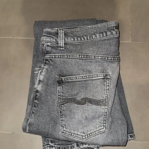 Grå jeans från Nudie Jeans - Snygga grå jeans från Nudie Jeans med en klassisk femficksdesign. De har en knappgylf och en diskret tvättad look som ger en cool stil. Perfekta för en avslappnad vardagslook.