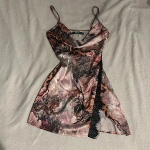 Leopard/ Blommig klänning från Missguided - Säljer en vacker blommig klänning från Missguided med tunna axelband och en elegant omlott-design. Klänningen har en fin spetsdetalj längs kanten och är perfekt för sommarens festligheter. Den har en kort längd och en härlig mix av rosa och beige toner.