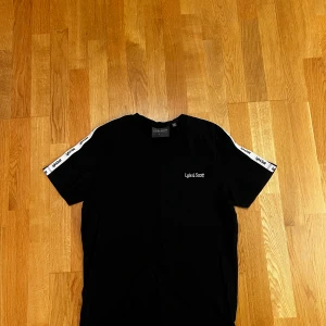 Svart t-shirt från Lyle & Scott - Snygg svart t-shirt från Lyle & Scott med vita detaljer längs ärmarna. 