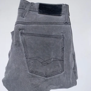 Replay Anbass  - Snygga grå jeans från Replay i modellen Anbass. De har en slim passform och är tillverkade i ett bekvämt bomullsmaterial. Byxorna har klassiska fem fickor och en knappgylf. Perfekta för en stilren look.