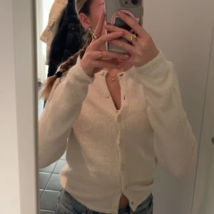 Vit kofta med knappar - Mysig vit kofta med knappar framtill. Perfekt för kyligare dagar och kan enkelt matchas med olika outfits. Den har en klassisk design med långa ärmar.