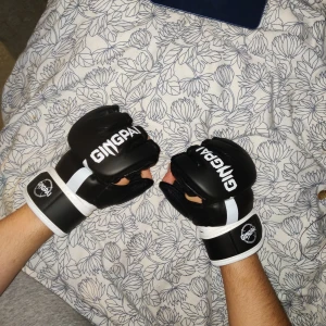 Svart/Vita mma handskar från Gingpai - Säljer ett par svart/vita mma handskar från Gingpai. Handskarna har öppen design för fingrarna och dubbel wrap för att skydda dina handleder. Mycket sköna och använda bara 3 gånger på boxningssäcken.
