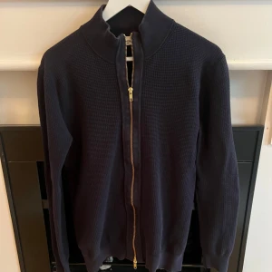 Helzip john Henric - Säljer en stilren mörkblå tröja från John Henric. Tröjan har en praktisk dragkedja framtill och är tillverkad i ett mjukt material. Perfekt för kyligare dagar.
