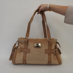 Beige handväska med pälsdetaljer - Snygg beige handväska med pälsdetaljer och silverfärgade metalldetaljer. Väskan har två handtag och praktiska sidofickor med lock och ringdetaljer. Perfekt för att ge din outfit en lyxig touch.💜