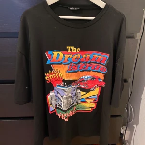 Svart t-shirt med tryck från Shein - Cool svart t-shirt från Shein med färgglatt tryck av bilar och texten 'The Dream is True'. Perfekt för en avslappnad stil med en touch av fart och fläkt.