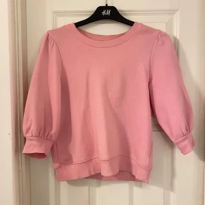 Rosa tröja från Gina Tricot - Säljer en söt rosa tröja från Gina Tricot med trekvartsärmar och ribbade muddar. Perfekt för en avslappnad stil. Tröjan har en rund halsringning och är gjord i ett mjukt material.