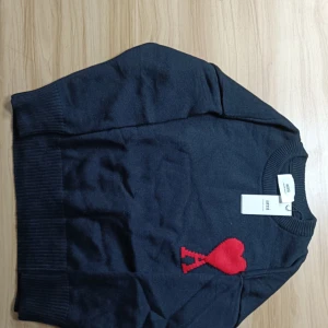 Ami paris sweater - Säljer en svart tröja från Ami Paris med ett rött hjärta på bröstet. Tröjan har långa ärmar och en rund halsringning. Perfekt för en stilren look. Helt my och oanvänd utomhus