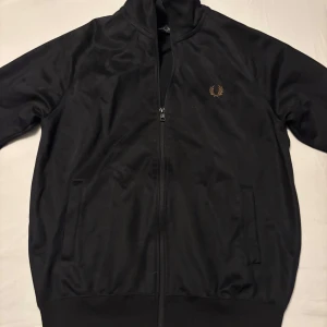  Fred Perry zip hoodie  - Säljer en stilren svart hoodie från Fred Perry med dragkedja. Den är använd ett fåtal gånger och har inga fläckar eller hål. Den har ett snyggt mönster på armarna.( Skick 10/10)